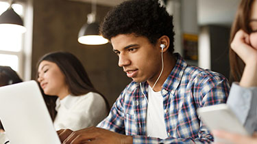 Male student working on laptop wearing headphones