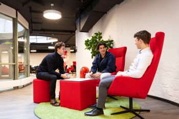 Three male students sitting in large red chairs on campus