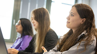 Three female students looking forward and listening to lecture in a classroom