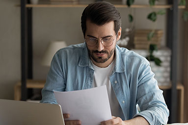 Male reading letter while sat infront of laptop